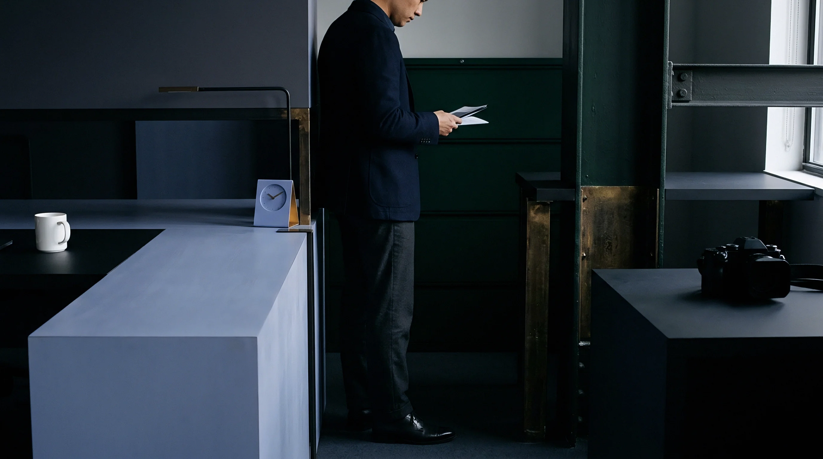 A business professional in a dark tailored jacket stands examining printed verification papers inside a minimalist industrial office space.