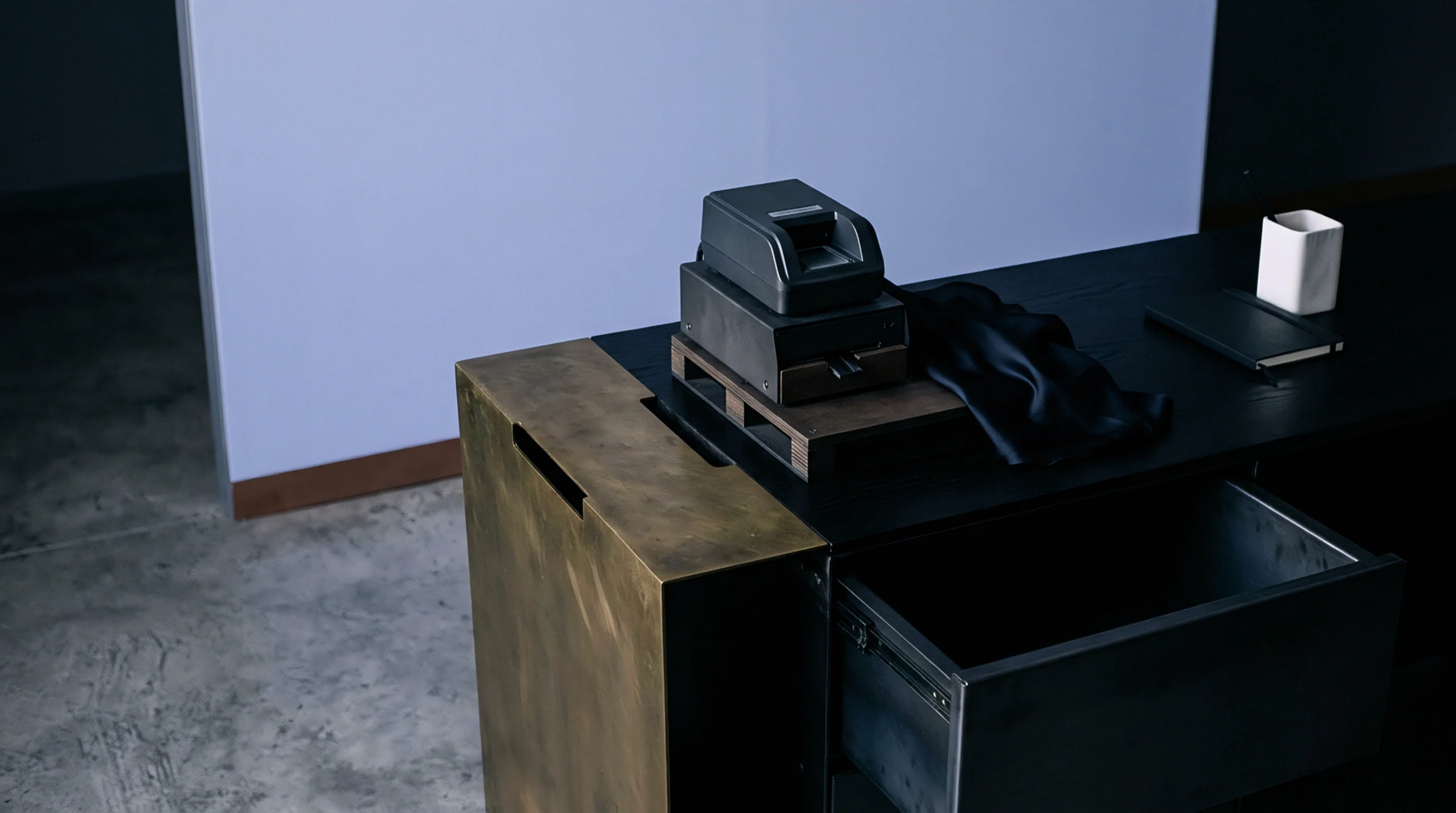 A black steel workstation features a thermal label printer resting on a wooden riser beside an open utility drawer in an industrial office.