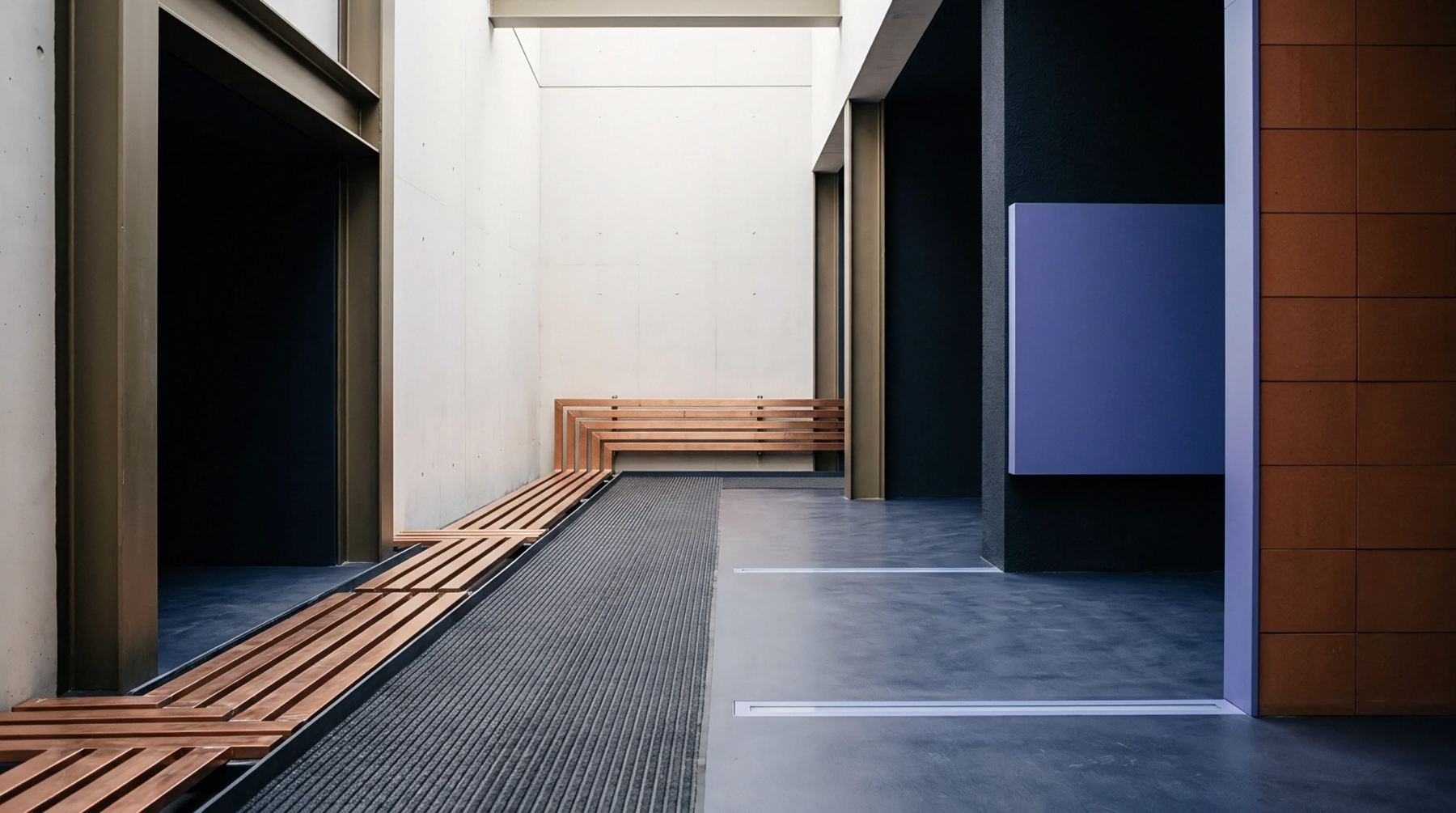 Industrial facility interior corridor features exposed concrete walls, steel structural columns, slatted timber benches, and grey composite flooring mats.