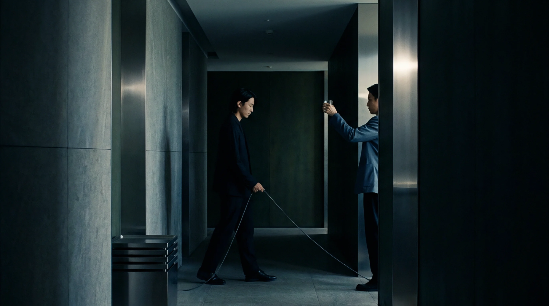 Two corporate figures in dark attire stand connected by a thin tether traversing a concrete and metallic industrial corridor.
